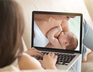 Mother breastfeeding baby during virtual consultation on laptop screen.