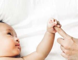 Baby reaching out to touch parent's finger.