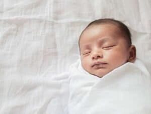 Baby sleeping peacefully wrapped in a white blanket.