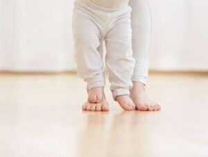 Close-up of a baby and adult's feet on a wooden floor, symbolizing support and care.